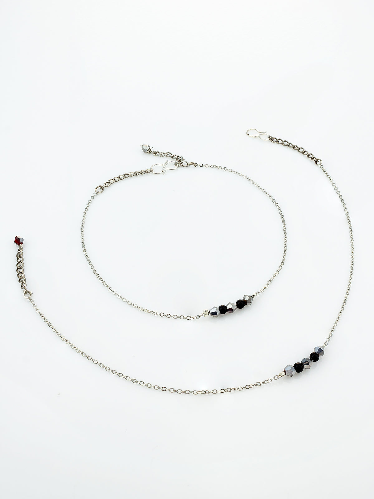 A delicate silver-toned chain anklet with small black and dark gray beads and a tiny red accent bead, displayed on a clean white background.