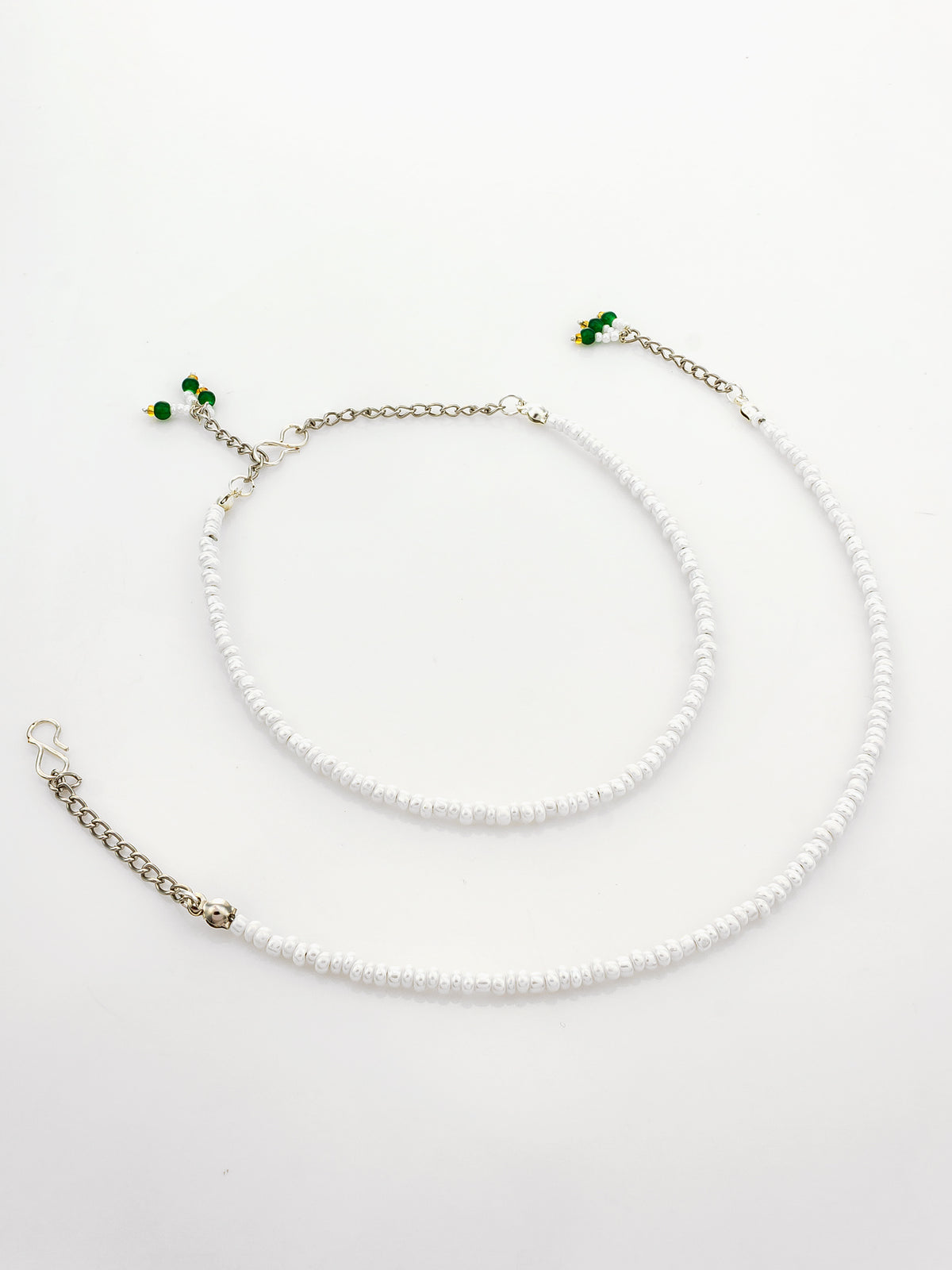 A white beaded ankle bracelet with silver-tone chain extender straps and small green bead accents, displayed on a clean white background.