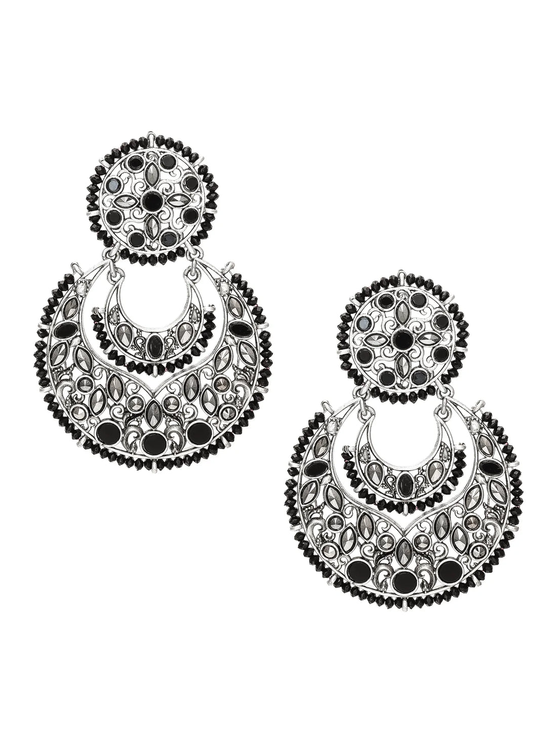 A pair of large silver-toned filigree earrings with circular and crescent-shaped designs, displayed on a carved wooden surface with draped green fabric in the background.