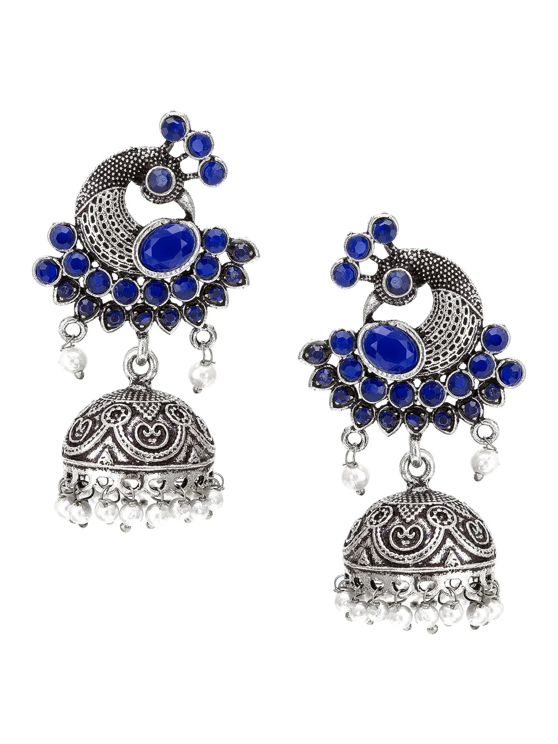 A pair of traditional Indian silver-toned jhumka earrings with deep blue stones and small white bead accents, displayed on a carved wooden block with draped green fabric in the background.