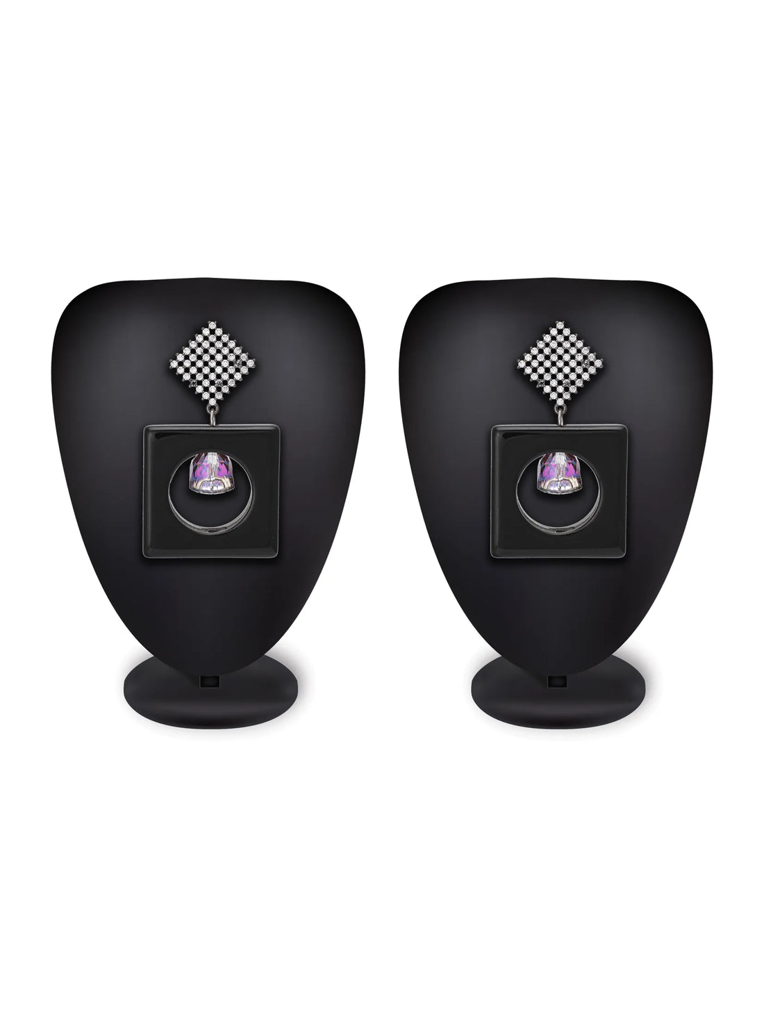 A pair of black square drop earrings with silver rhinestone-embellished posts and a faceted iridescent gemstone in the center, displayed on a white plate over a turquoise background.