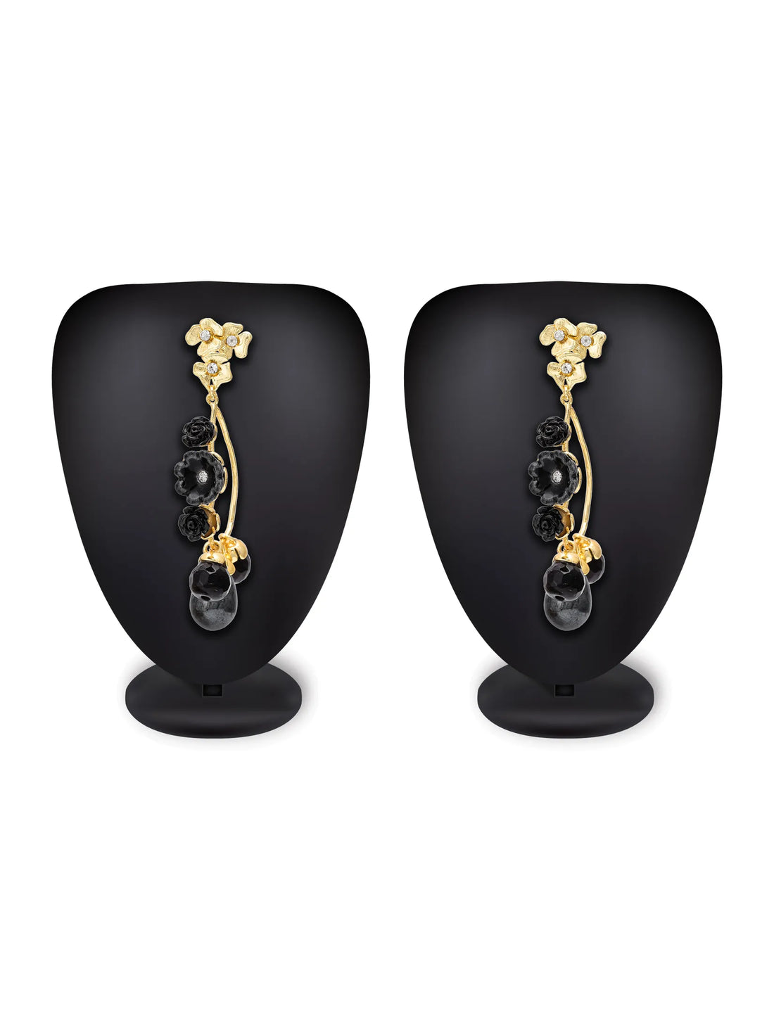 Gold-tone drop earrings with black faceted beads and crystal accents, displayed on a bright turquoise background with decorative floral props.