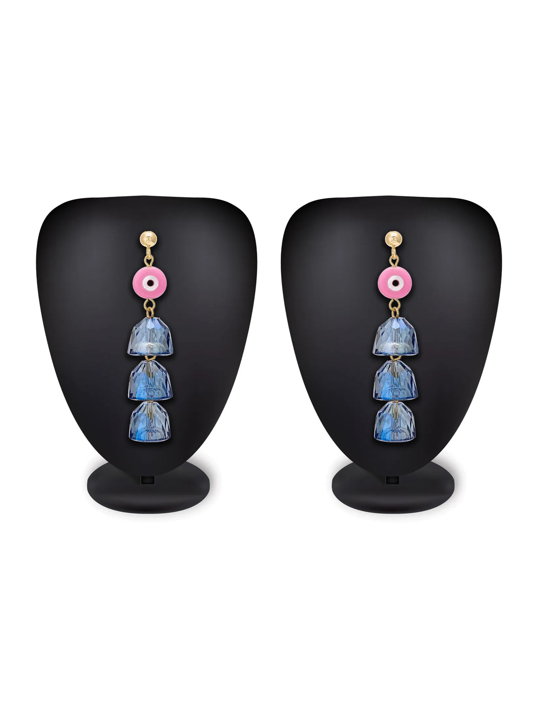 A pair of dangling earrings with gold-tone posts, pink evil eye charms, and three faceted dark blue beads, displayed on a turquoise background with a white plate and a peach flower prop.