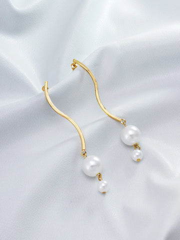 Gold-tone wavy hoop earrings with dangling white pearl drops, displayed on a soft white satin fabric background.