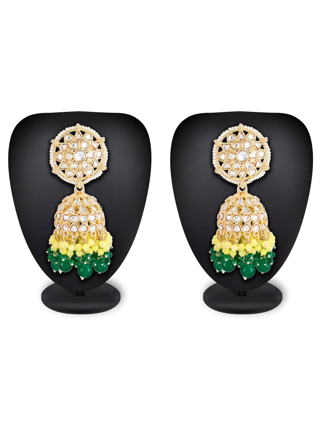 Gold-plated Indian jhumka earrings with white stones, yellow beads, and green bead drops, displayed on a carved wooden block.