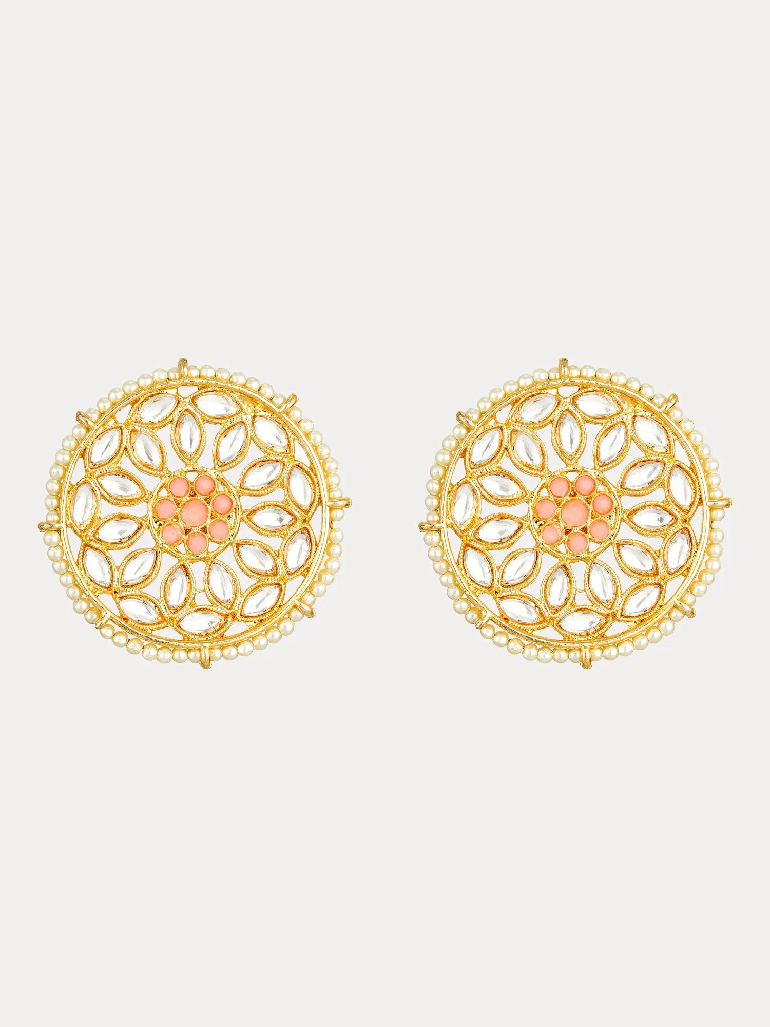 A pair of gold-toned circular stud earrings with intricate filigree cutouts, a border of small white stones, and a central peach-pink floral motif, shown on a light gray background.