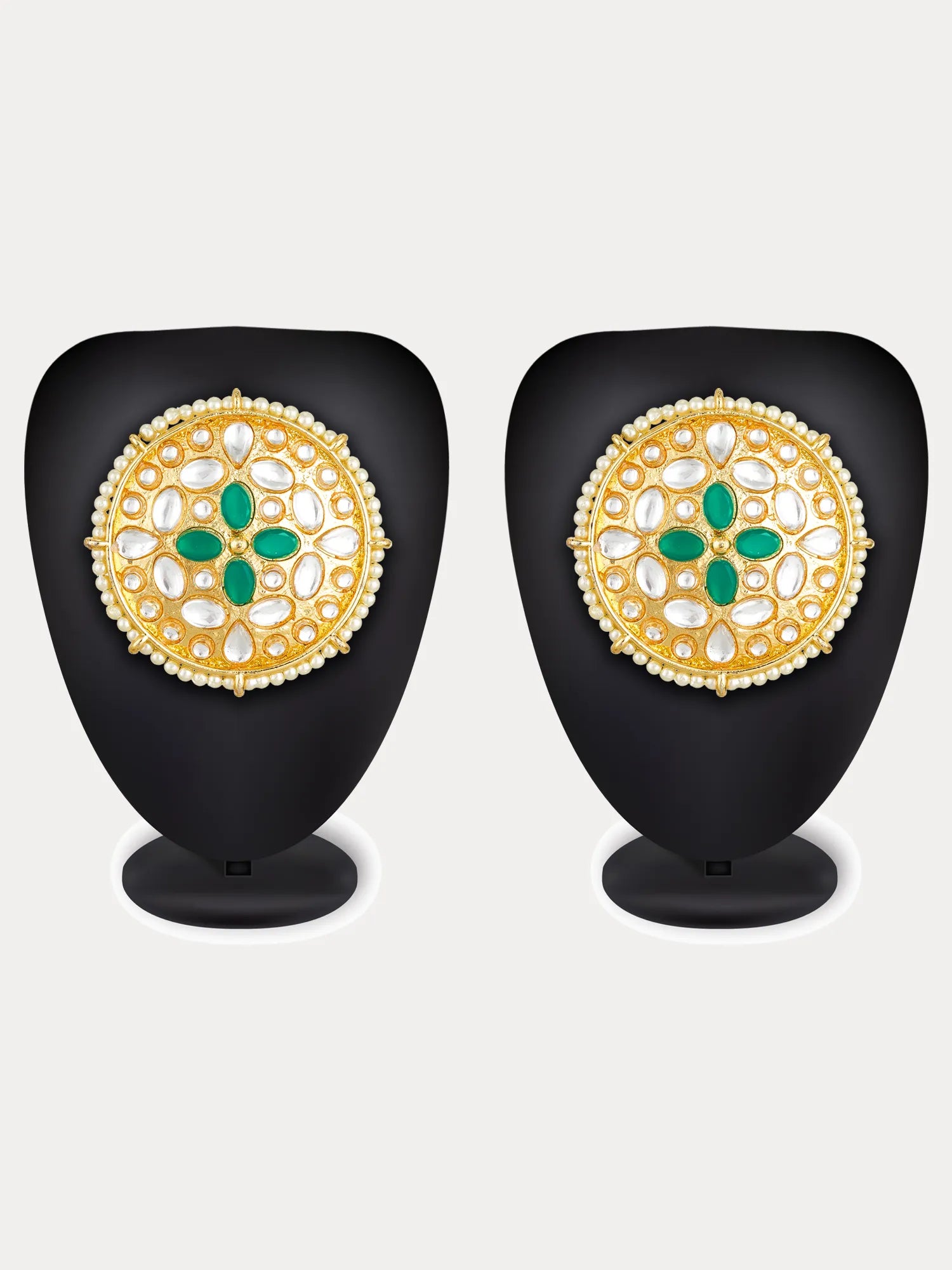 A pair of ornate gold circular earrings displayed on black mannequin busts against a light gray background. Each earring features a gold circular design with a central green floral motif and white stone accents.