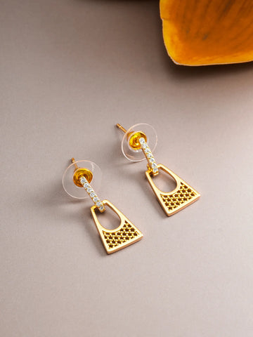 A pair of gold geometric drop earrings with clear crystal accents, displayed on a neutral gray surface with a yellow decorative element in the top right corner.