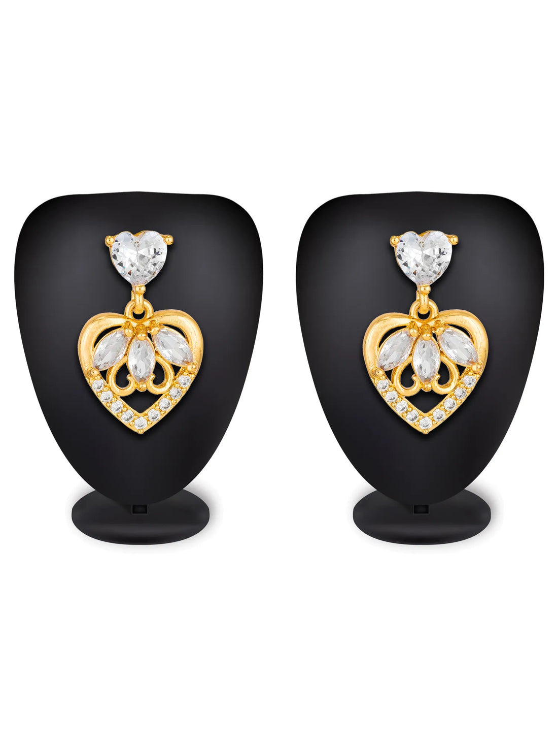 A pair of gold heart-shaped stud earrings with clear crystal drops, displayed on a neutral gray surface with a yellow flower in the background.