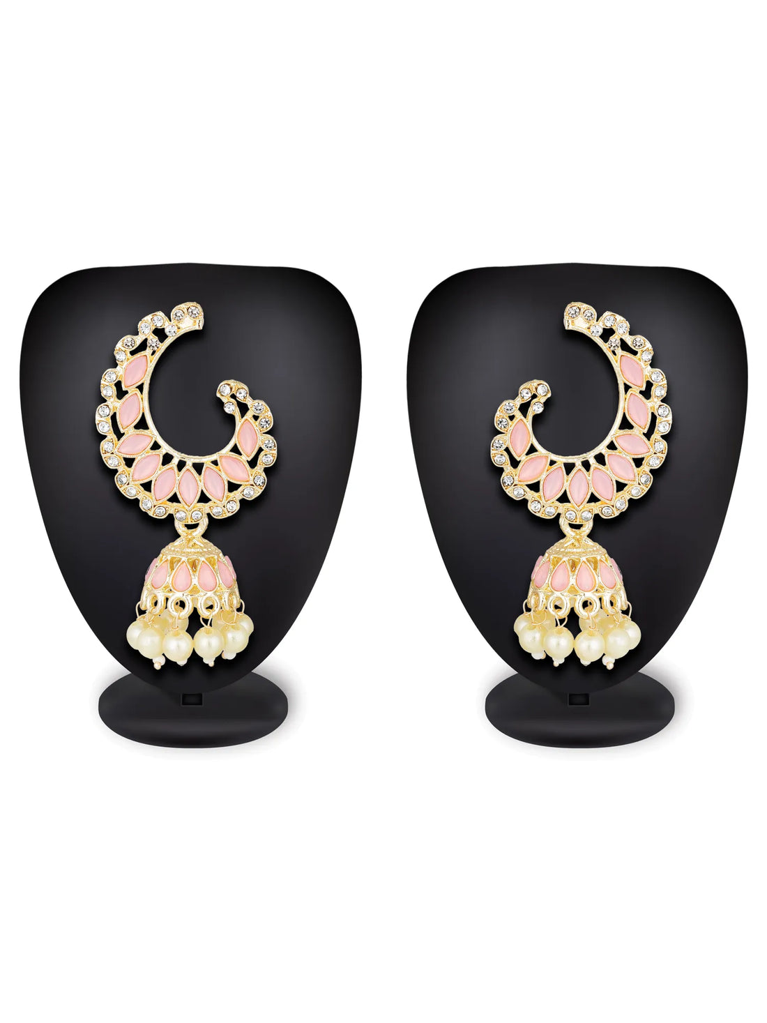 A pair of gold-plated crescent-shaped jhumka earrings with pink enamel details, clear rhinestones, and dangling cream pearl clusters, displayed on a textured pink surface with red roses in the corner.