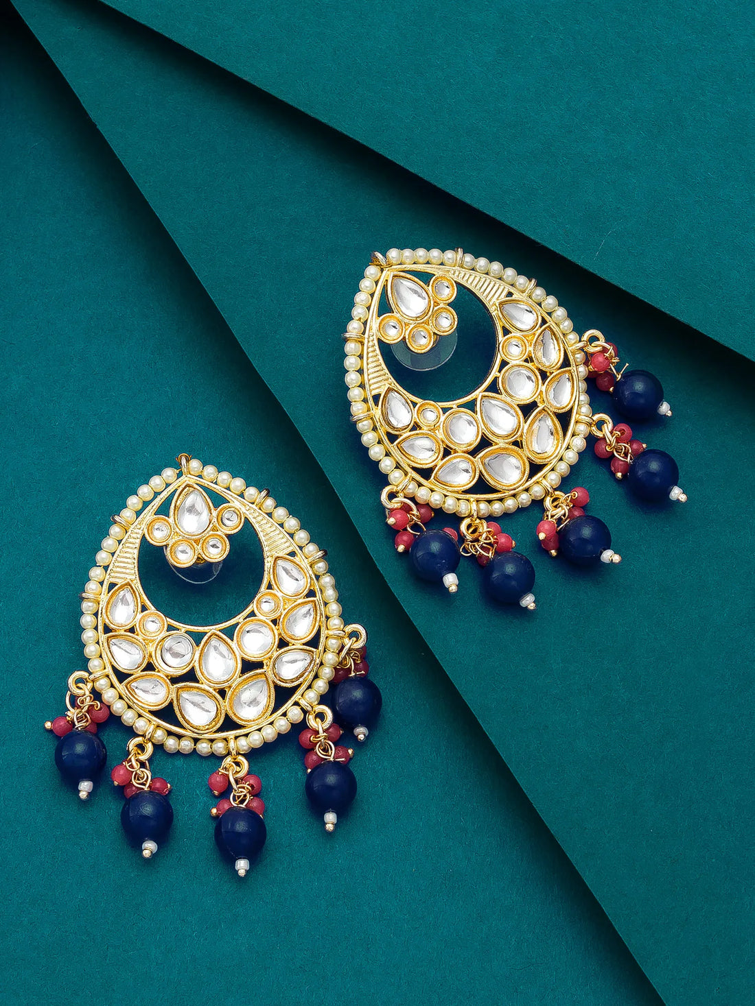 Ornate earrings with gold, blue, and red elements on a teal background