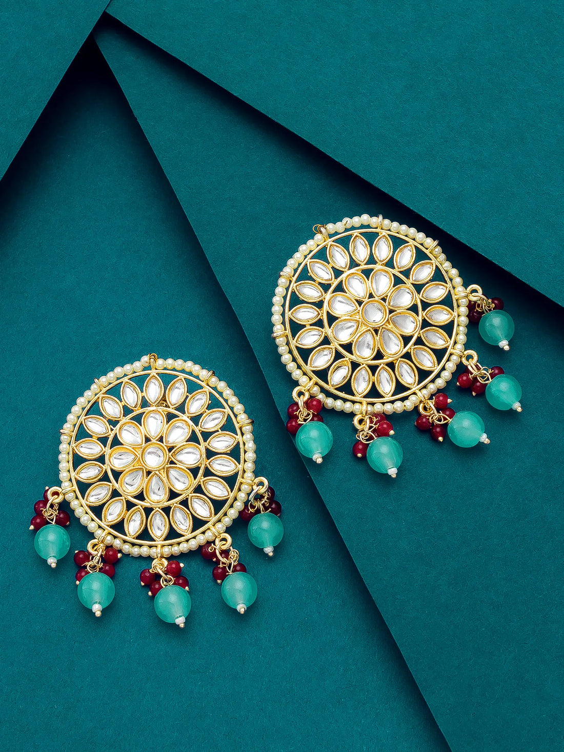 Ornate gold earrings with turquoise and red beads on a teal background
