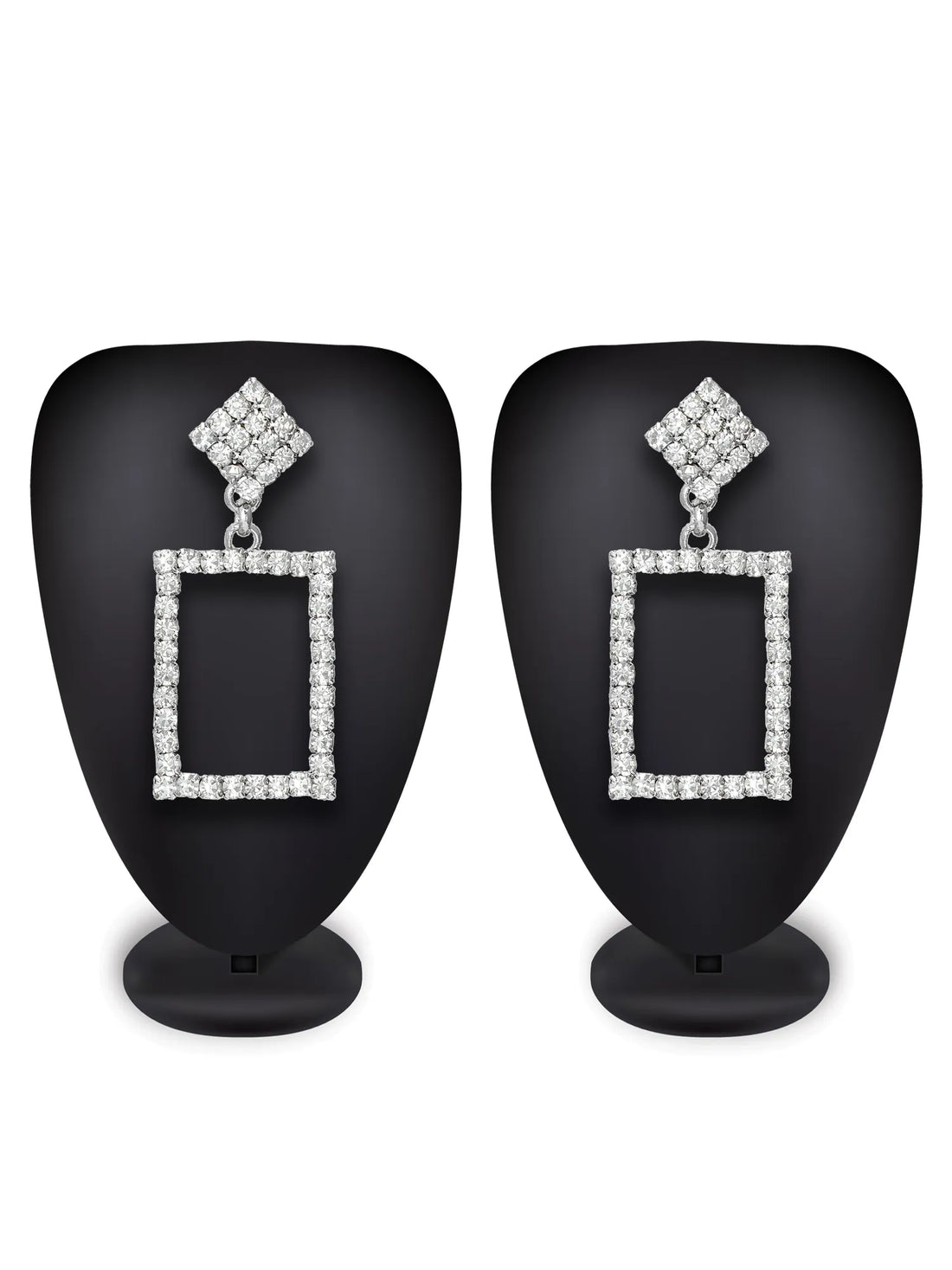 A pair of silver-tone drop earrings with square-shaped rectangular frames paved with clear cubic zirconia stones, resting on a draped deep red satin fabric background.