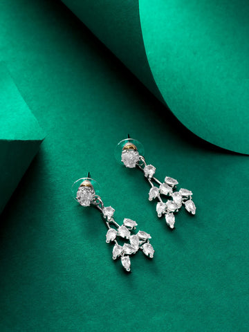 A pair of silver-toned dangle earrings with clear marquise-cut gemstones arranged in a leafy cluster design, displayed on a dark green textured background.