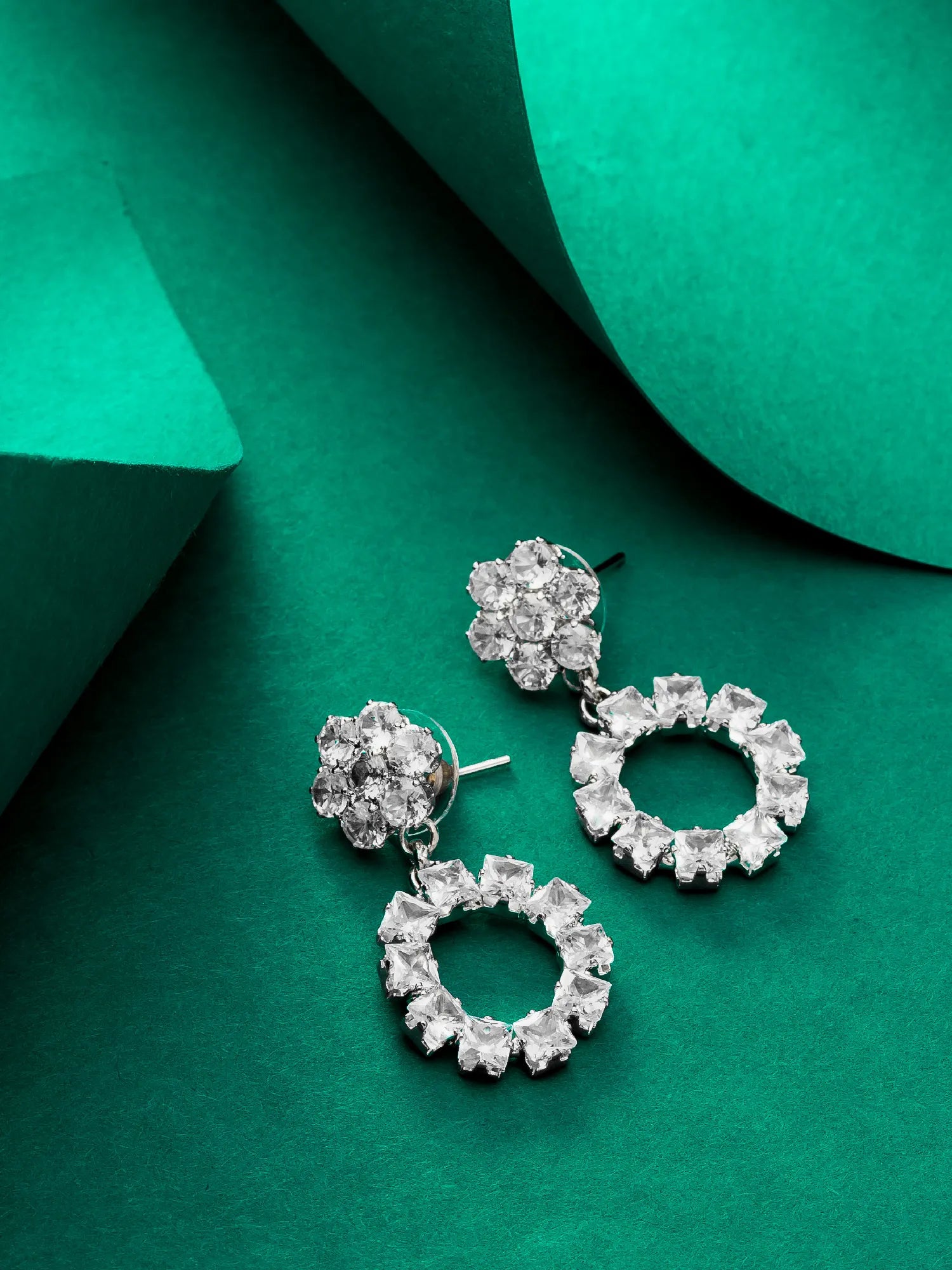 Pair of silver hoop earrings with clear gemstones on a green background