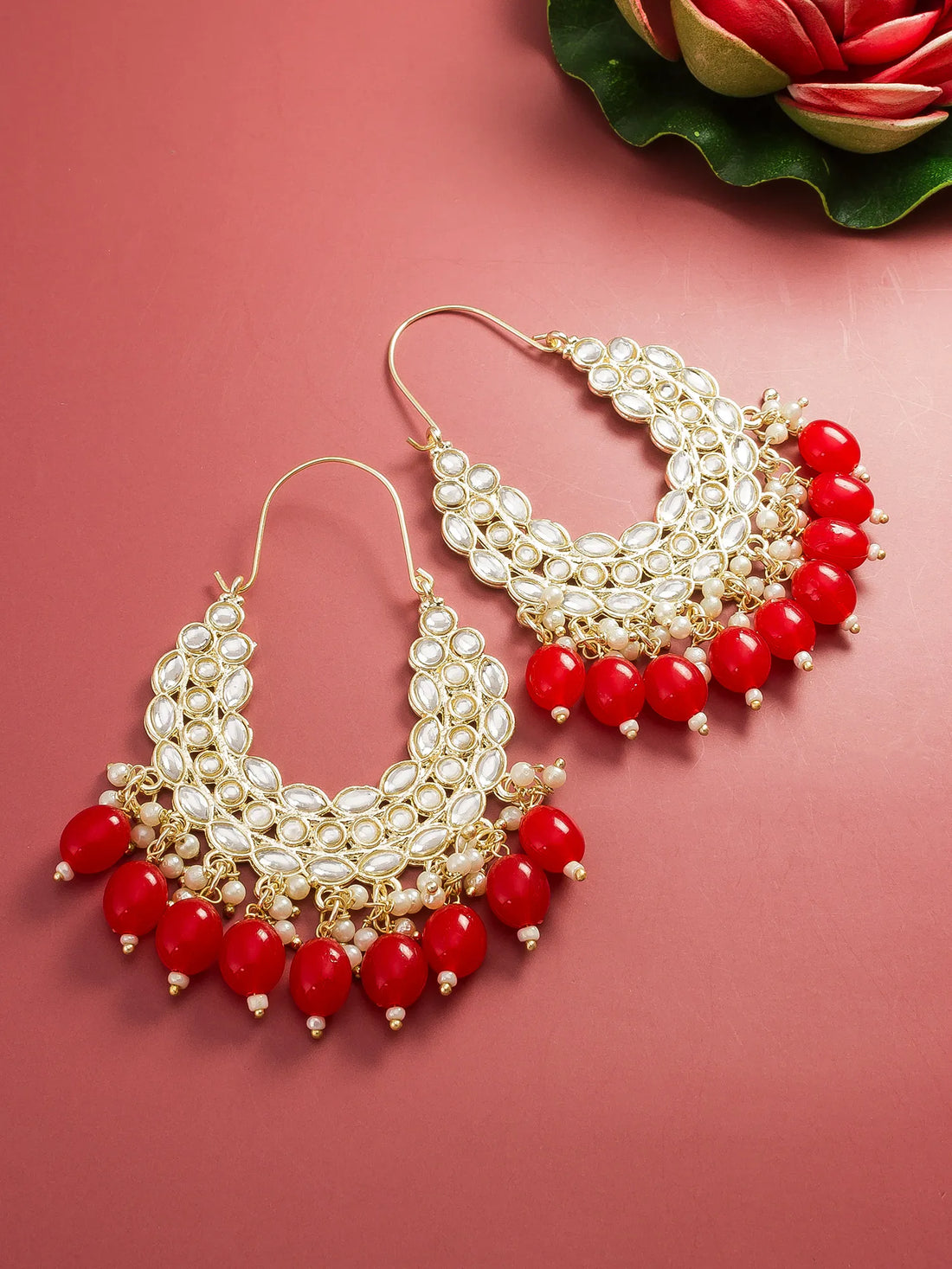 Pair of earrings with red beads and pearl-like stones on a pink background