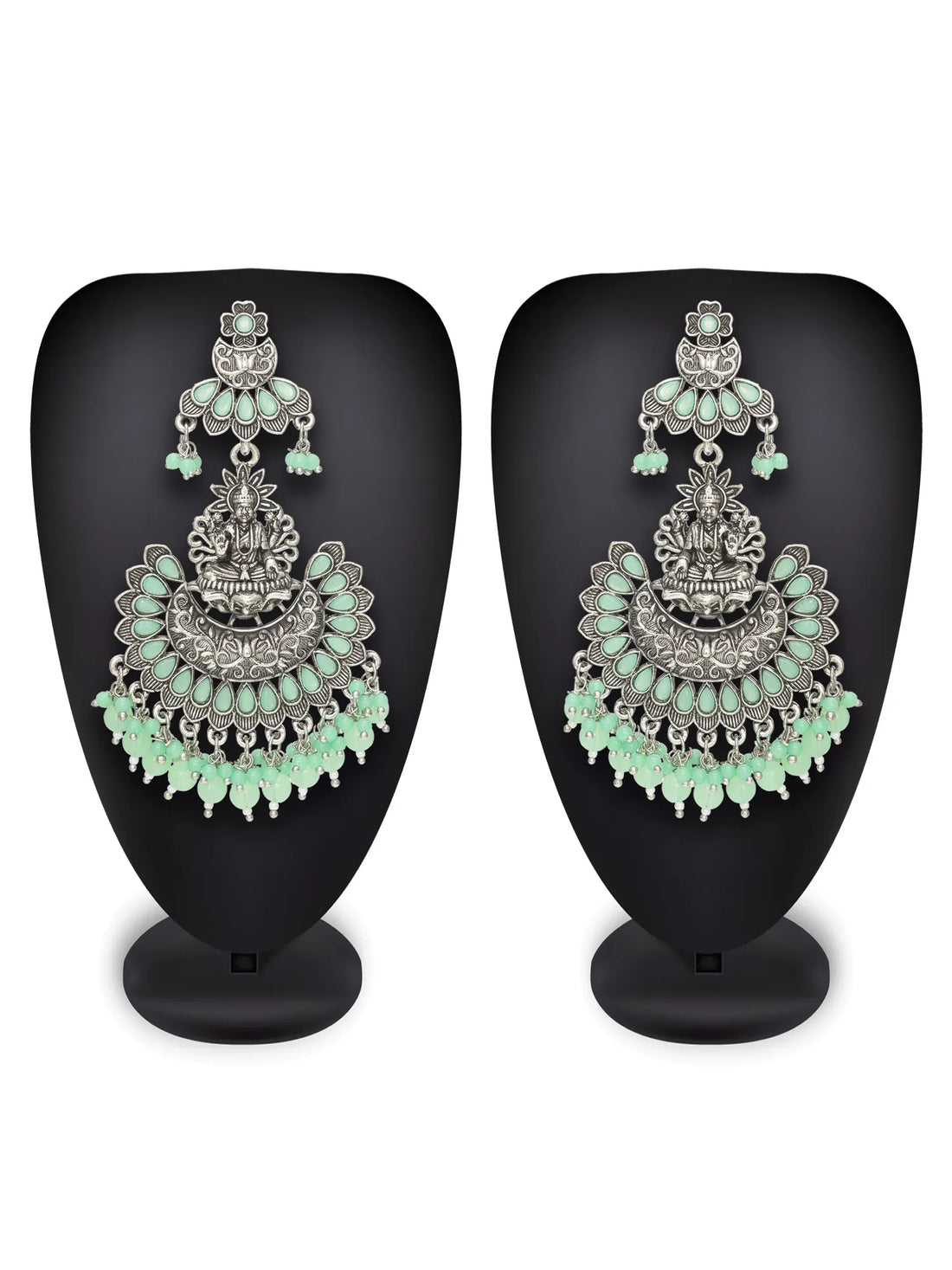 Ornate silver and green earrings on a dark surface with green fabric background