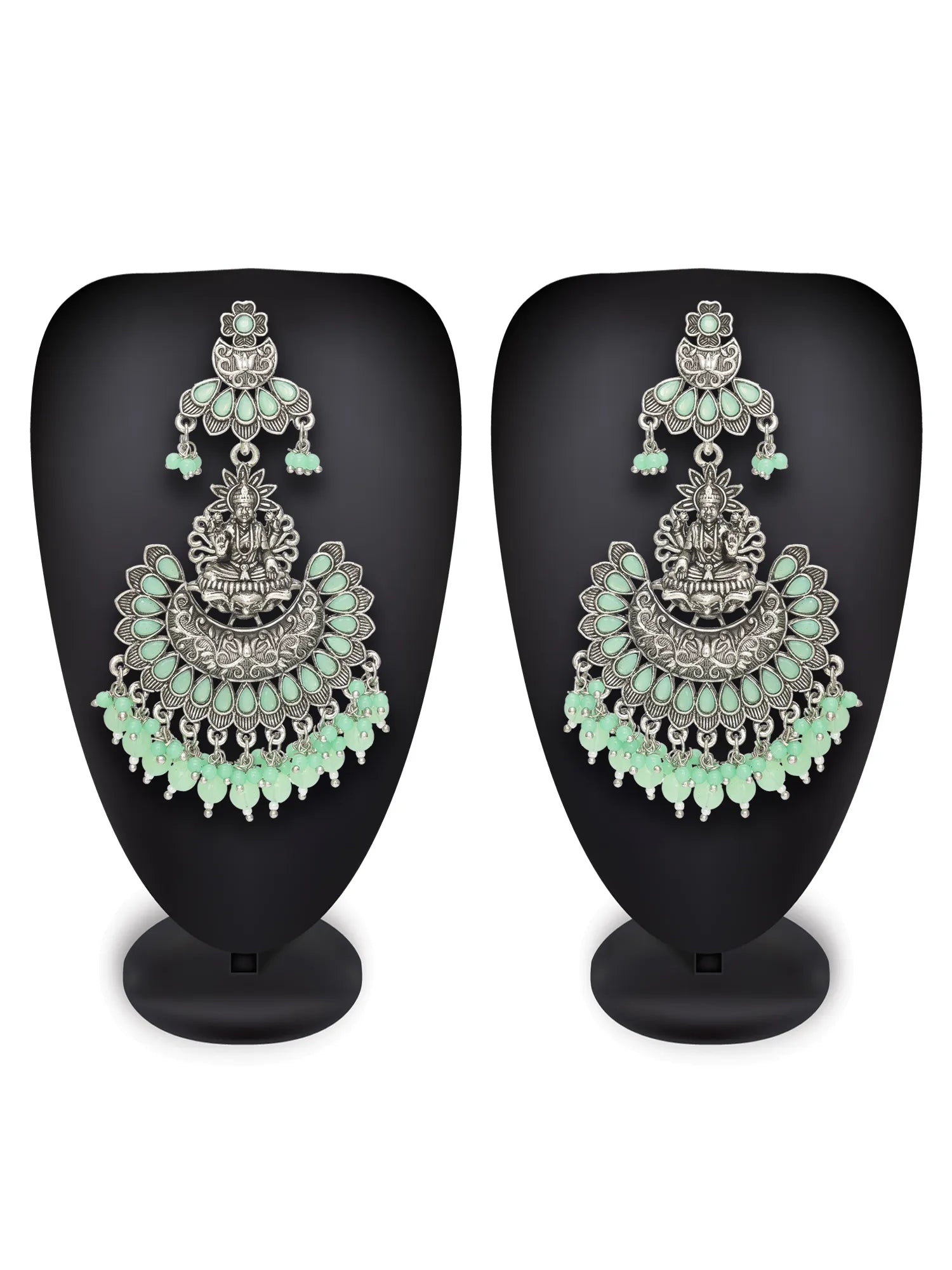 A pair of ornate silver-toned Indian jhumka earrings embellished with light green stones, displayed on black mannequin busts against a white background.