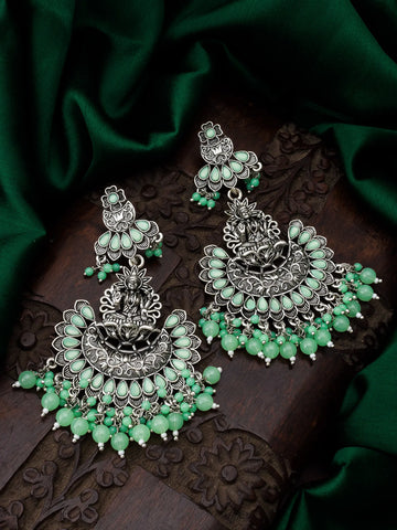 Ornate silver and green earrings on a dark surface with green fabric background