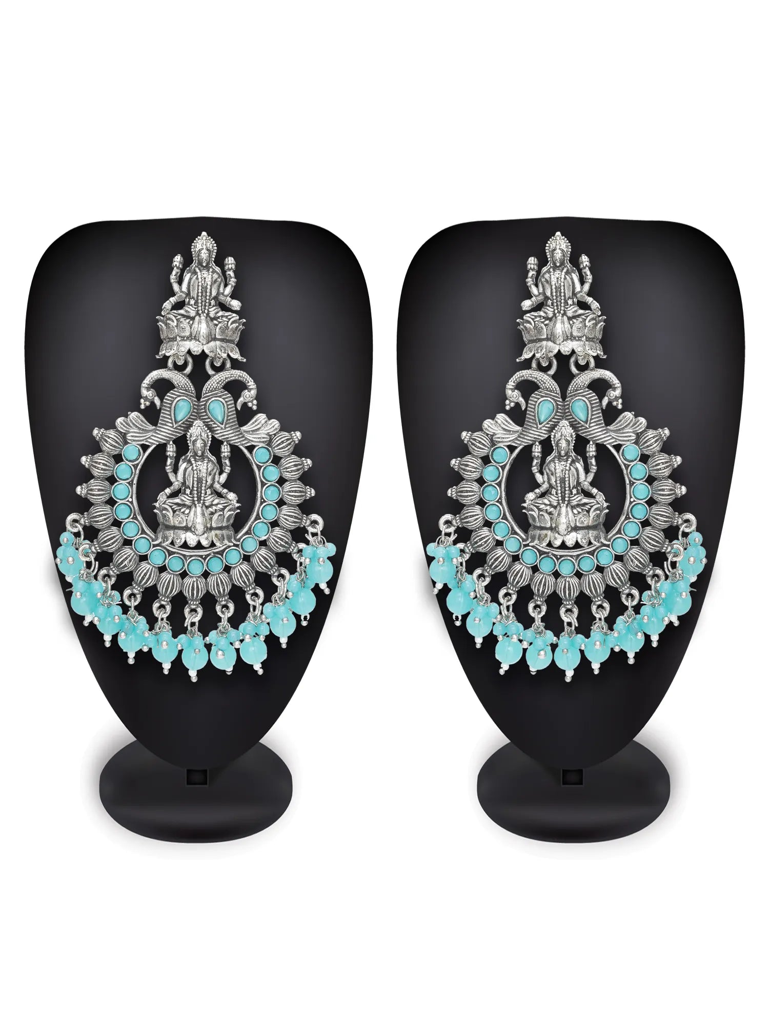 A pair of ornate silver-toned statement earrings displayed on black mannequin busts against a white background. The earrings feature detailed silver filigree, a central deity motif, and rows of turquoise blue stones.