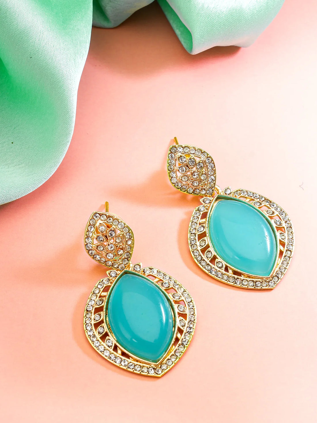Turquoise earrings with gold accents on a pink and green background