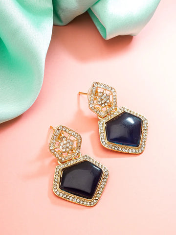 Gold and black earrings on a pink surface with a green fabric background