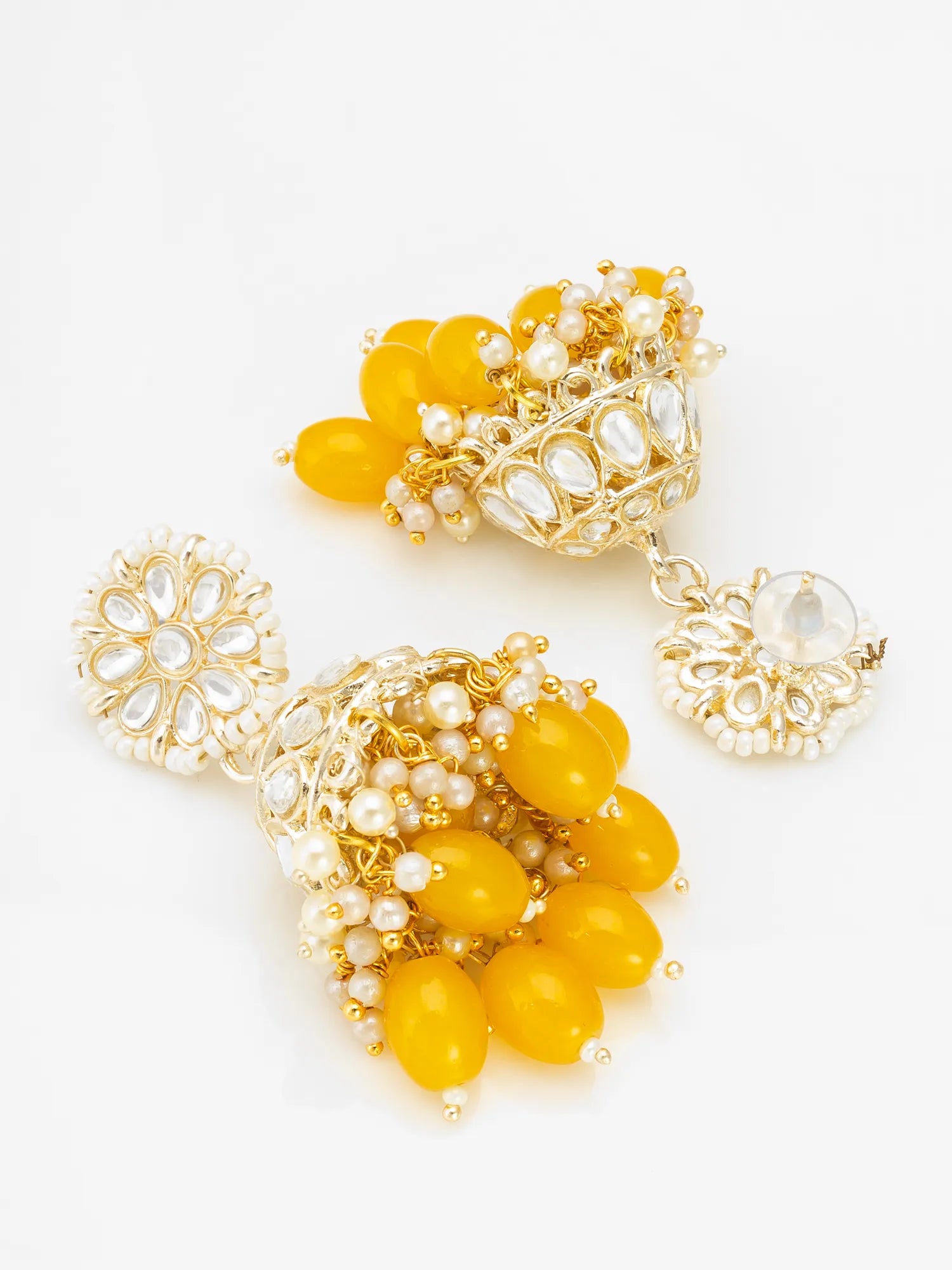 A pair of ornate gold-toned jhumka earrings decorated with yellow beads, white faux pearls, and clear rhinestones, displayed on a clean white background.