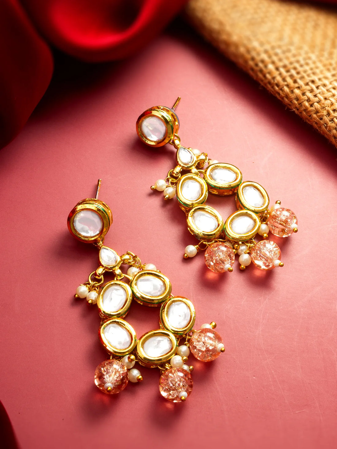 Gold and pink earrings on a pink surface with a red and gold background