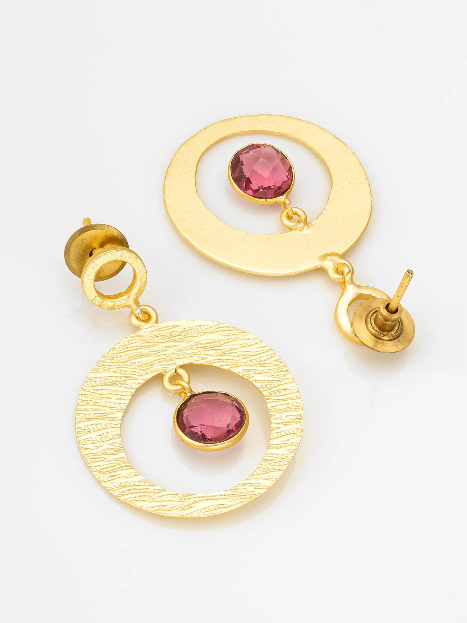A pair of gold-toned dangle earrings with circular cutouts and oval pink gemstones, displayed on a clean white background.