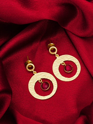 Gold earrings with red gemstones on a red fabric background