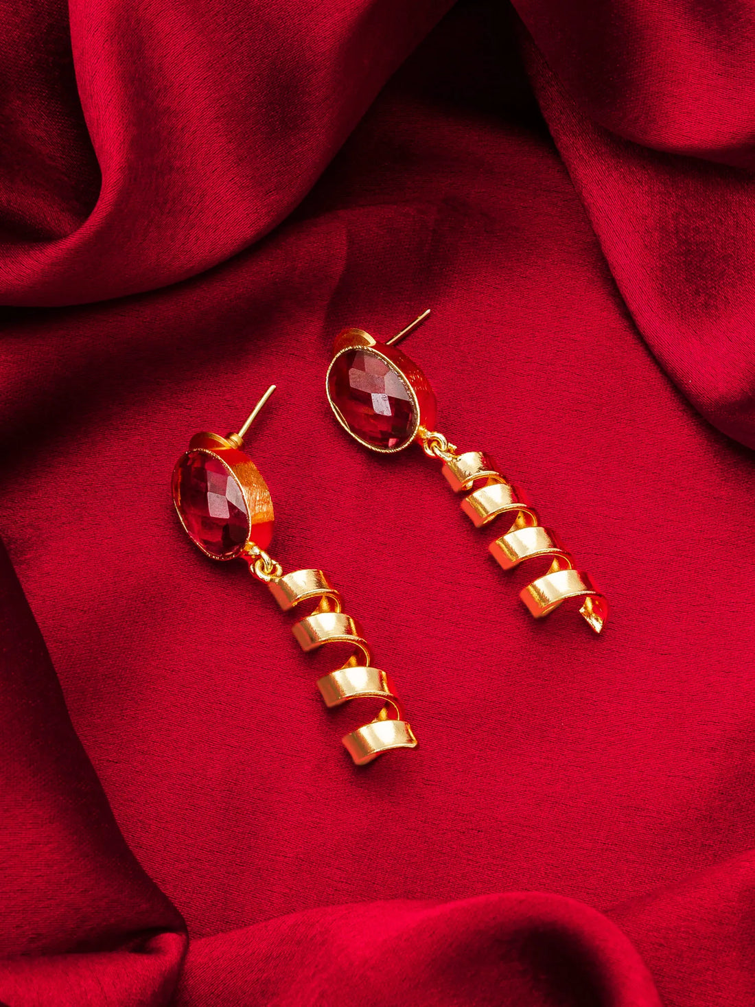 Gold earrings with red gemstones on a red fabric background
