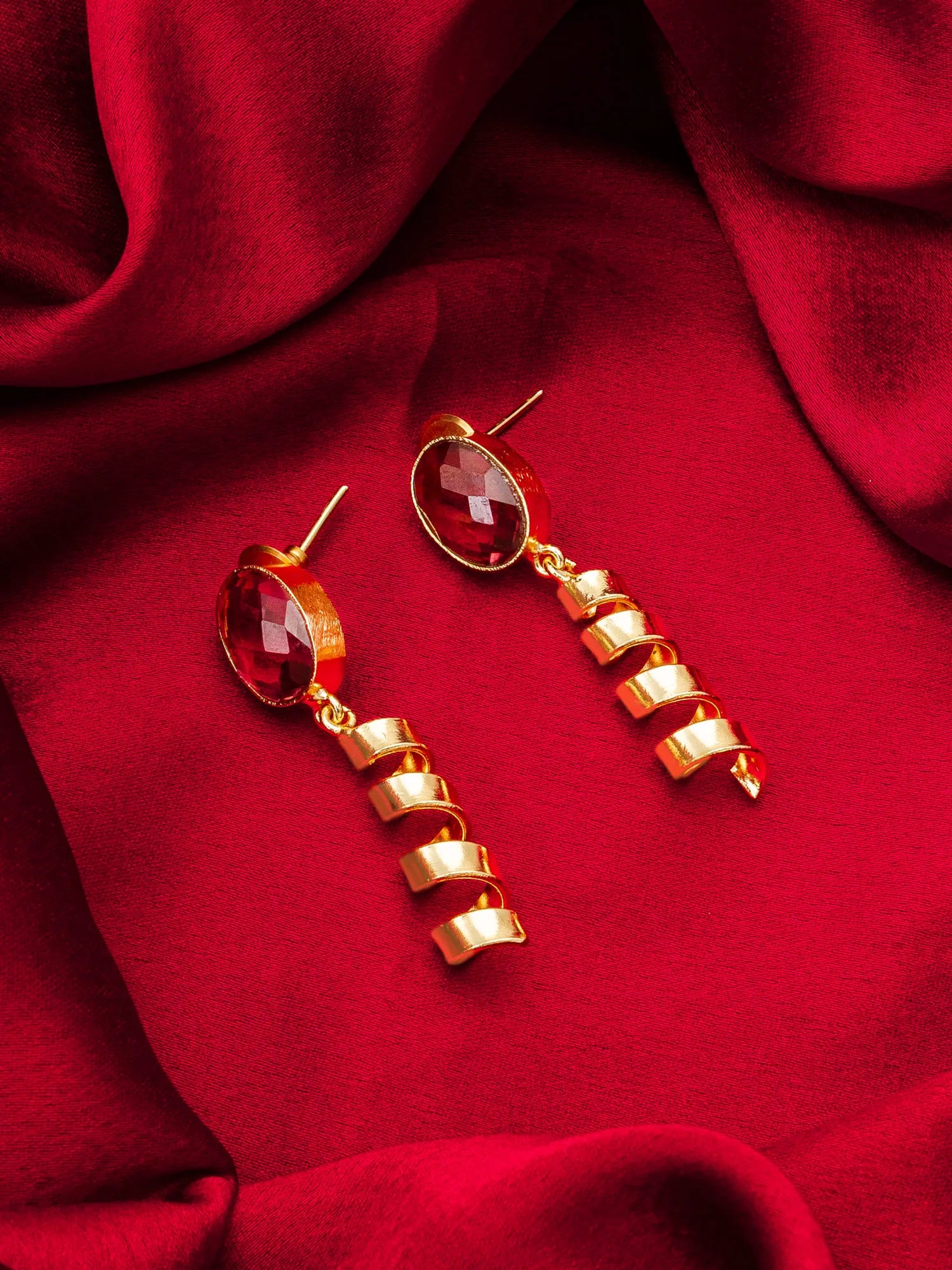 Gold earrings with red gemstones on a red fabric background