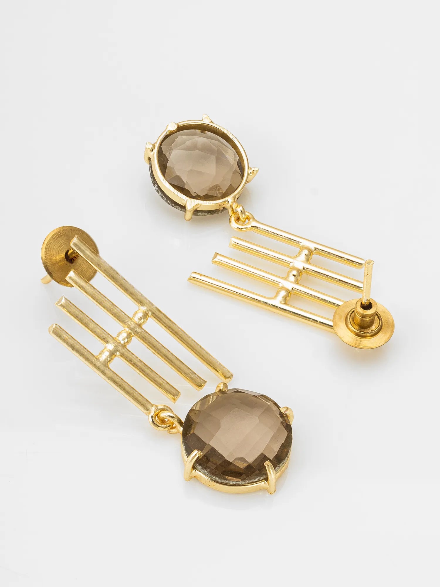 A pair of gold drop earrings with a faceted smoky brown gemstone in a round bezel setting, suspended from geometric gold bars, shown on a light gray background.