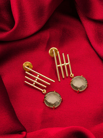 A pair of gold-toned statement earrings with geometric bar details and oval smoky gray-green gemstones, displayed on a draped red fabric background.