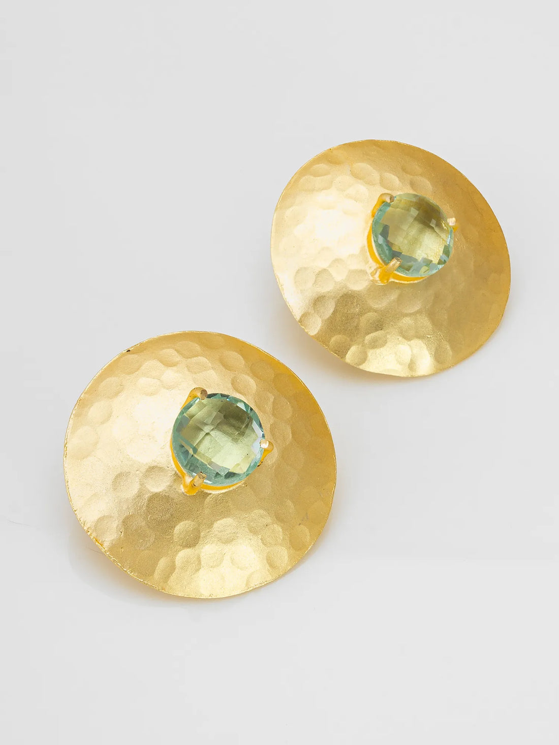 Two hammered gold-tone oval earrings with central clear gemstones, arranged on draped red fabric.