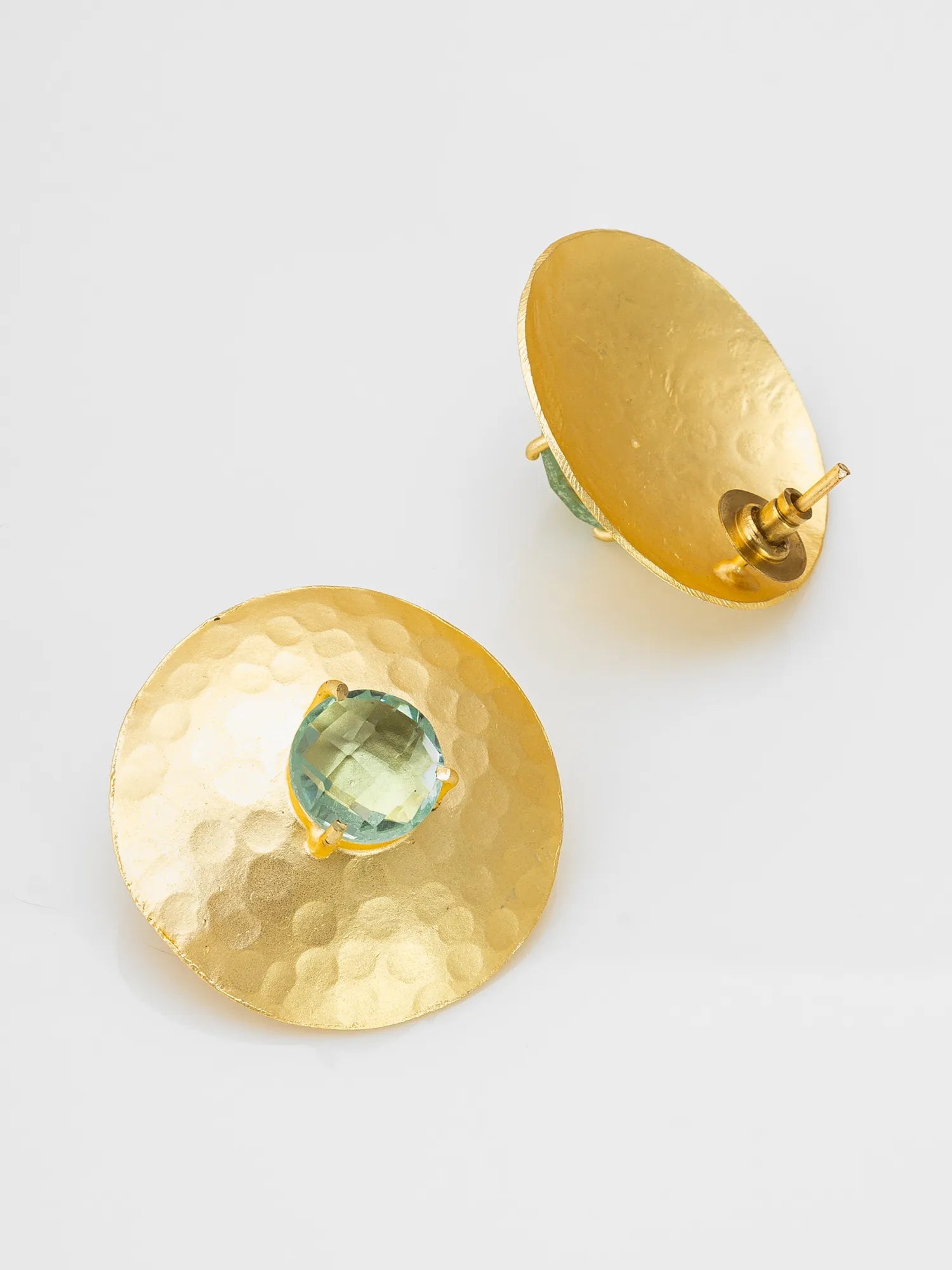 A pair of gold-toned hammered disc earrings with a round light blue-green gemstone at the center, displayed on a clean white background.