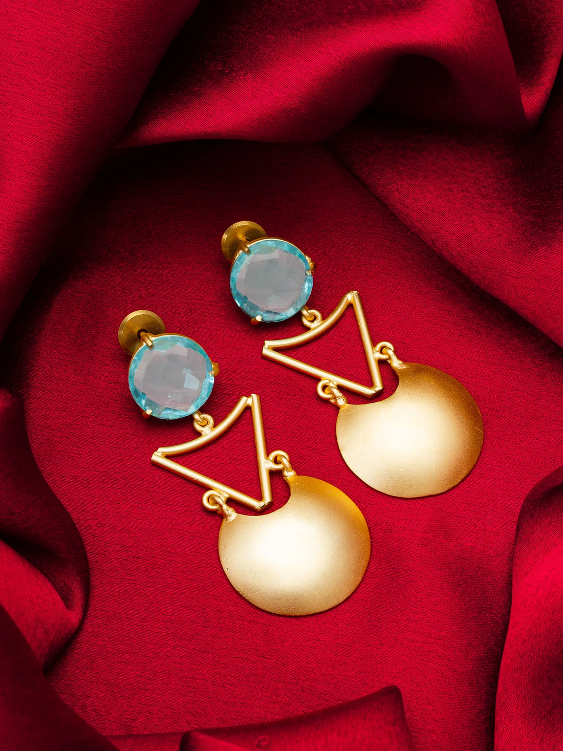 Gold and blue earrings on a red fabric background