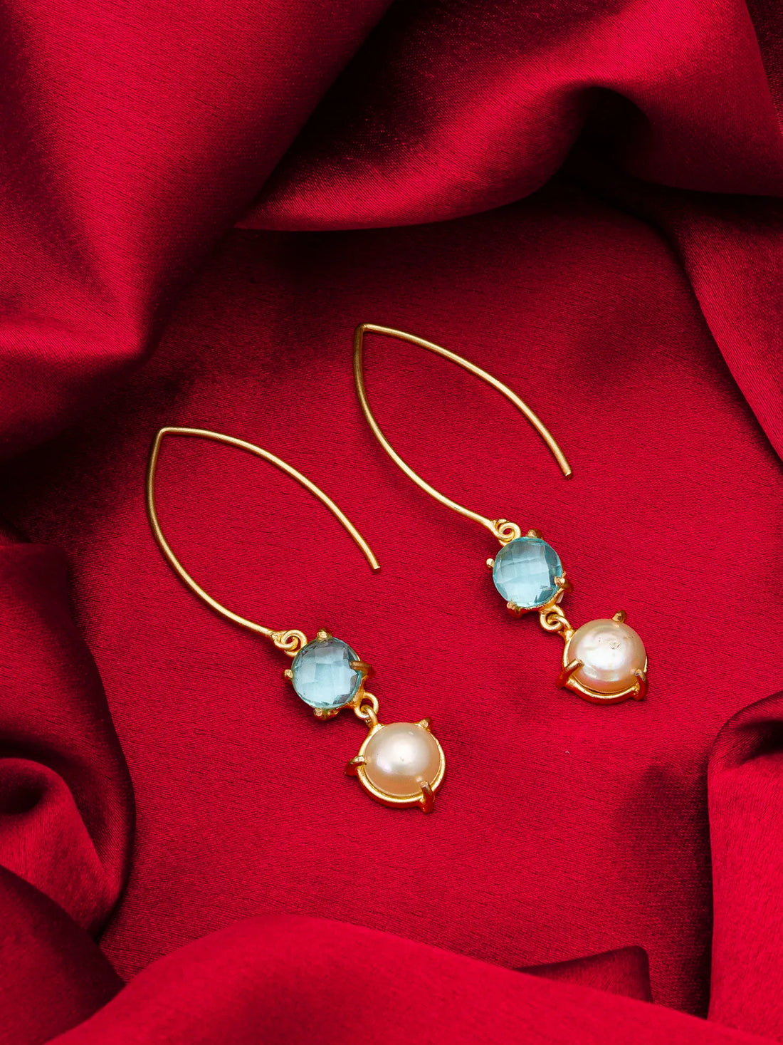 Gold earrings with blue and pearl drops on a red fabric background