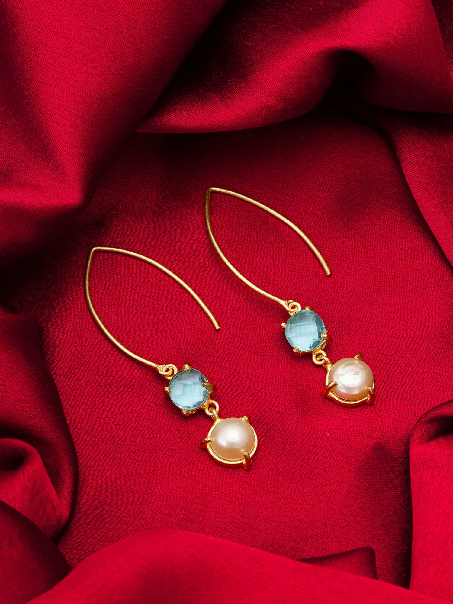 Gold earrings with blue and pearl drops on a red fabric background