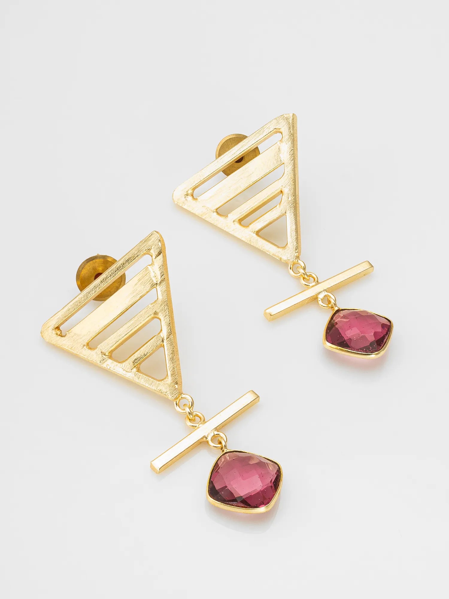 Gold geometric dangle earrings with triangular cutout tops, horizontal bar drops, and faceted pink gemstone pendants on a light gray background.