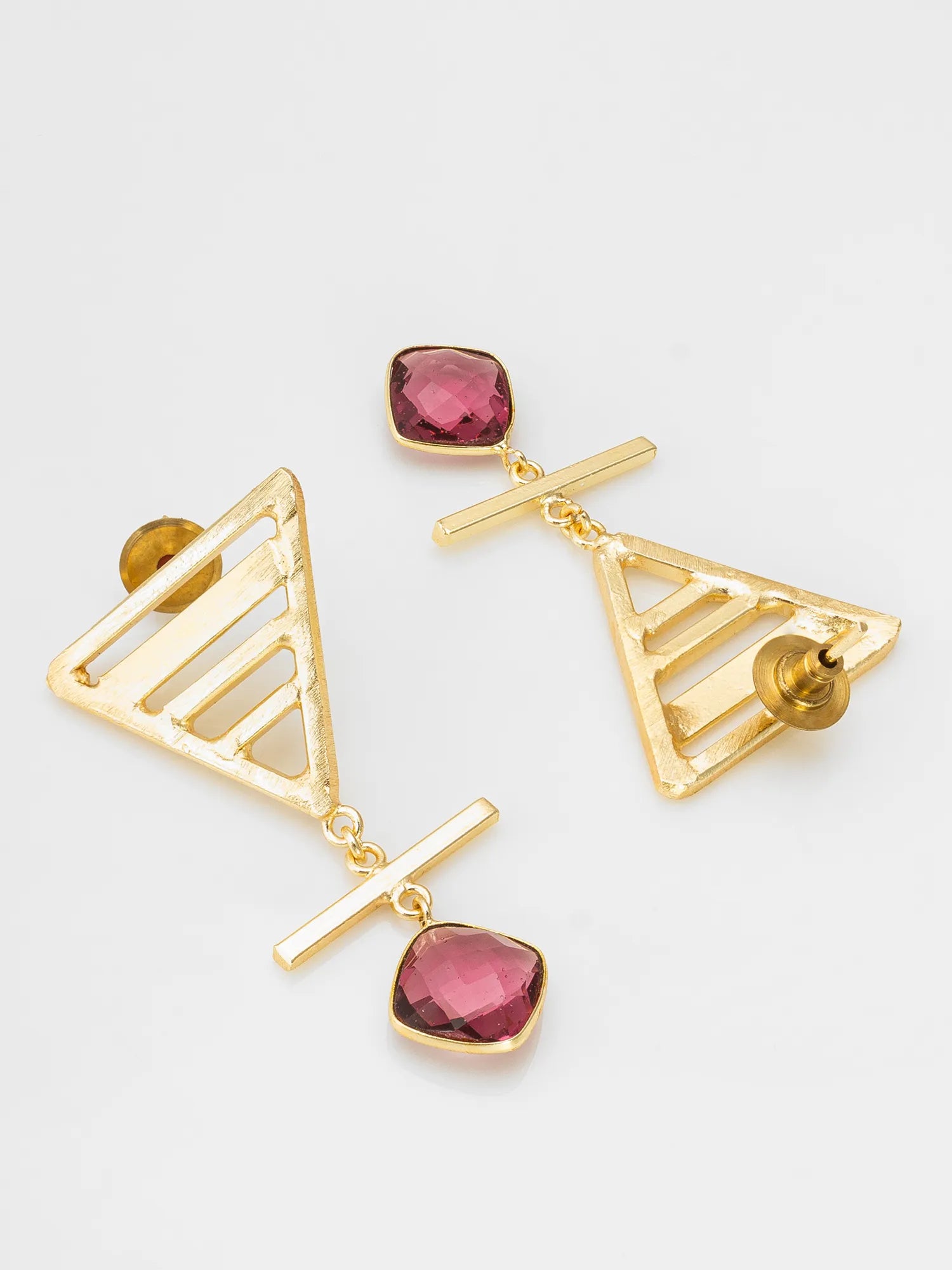 A pair of gold geometric drop earrings featuring triangular cutout frames, horizontal bar details, and faceted pink gemstone charms, displayed on a light gray background.