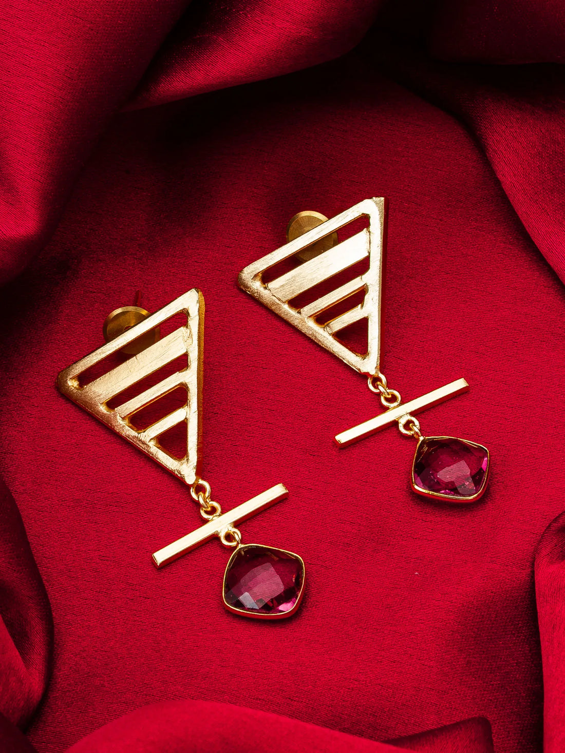 Gold earrings with red gemstones on a red fabric background