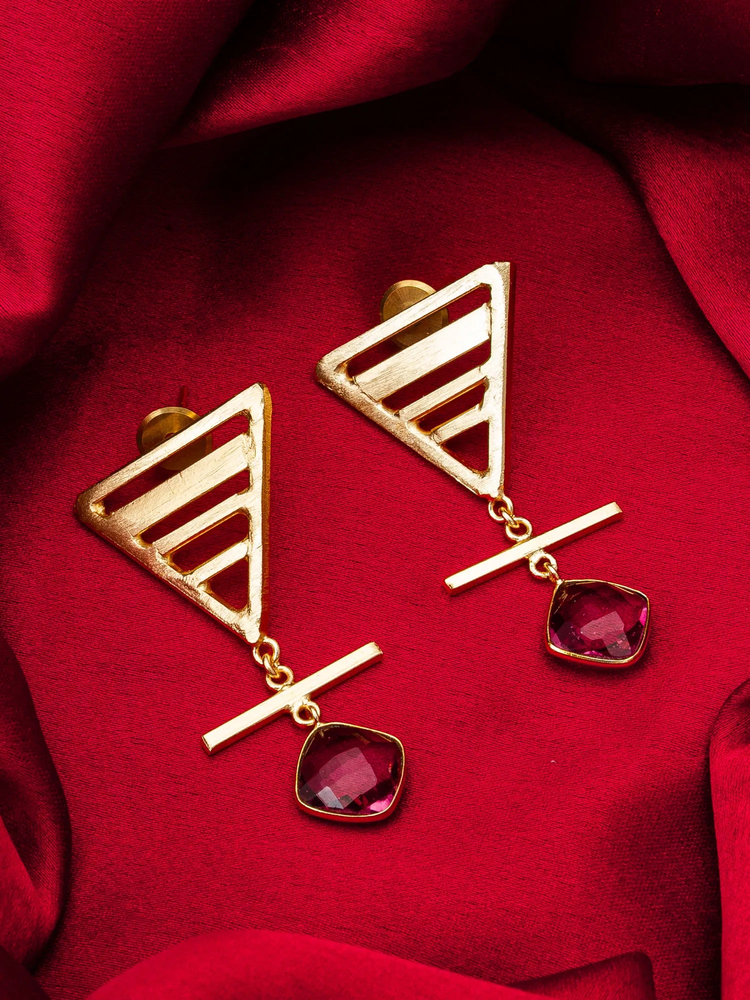 Gold earrings with red gemstones on a red fabric background