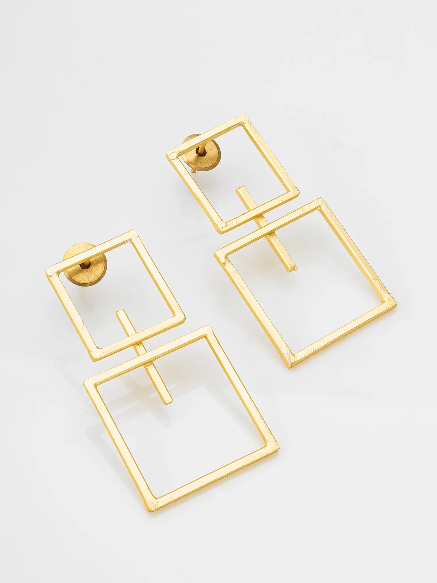 A pair of gold-toned geometric drop earrings with nested square frames and a central crossbar, photographed on a clean white background.