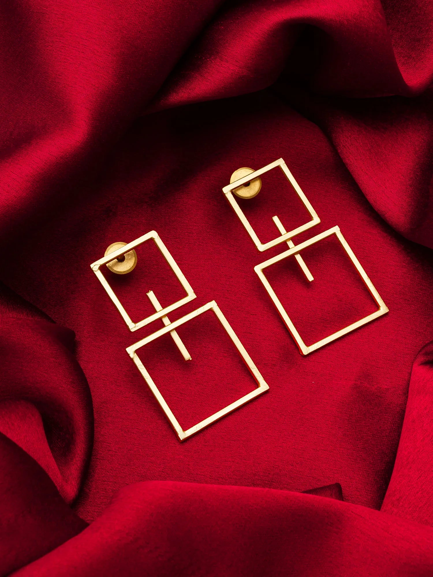 Gold square earrings on a red fabric background