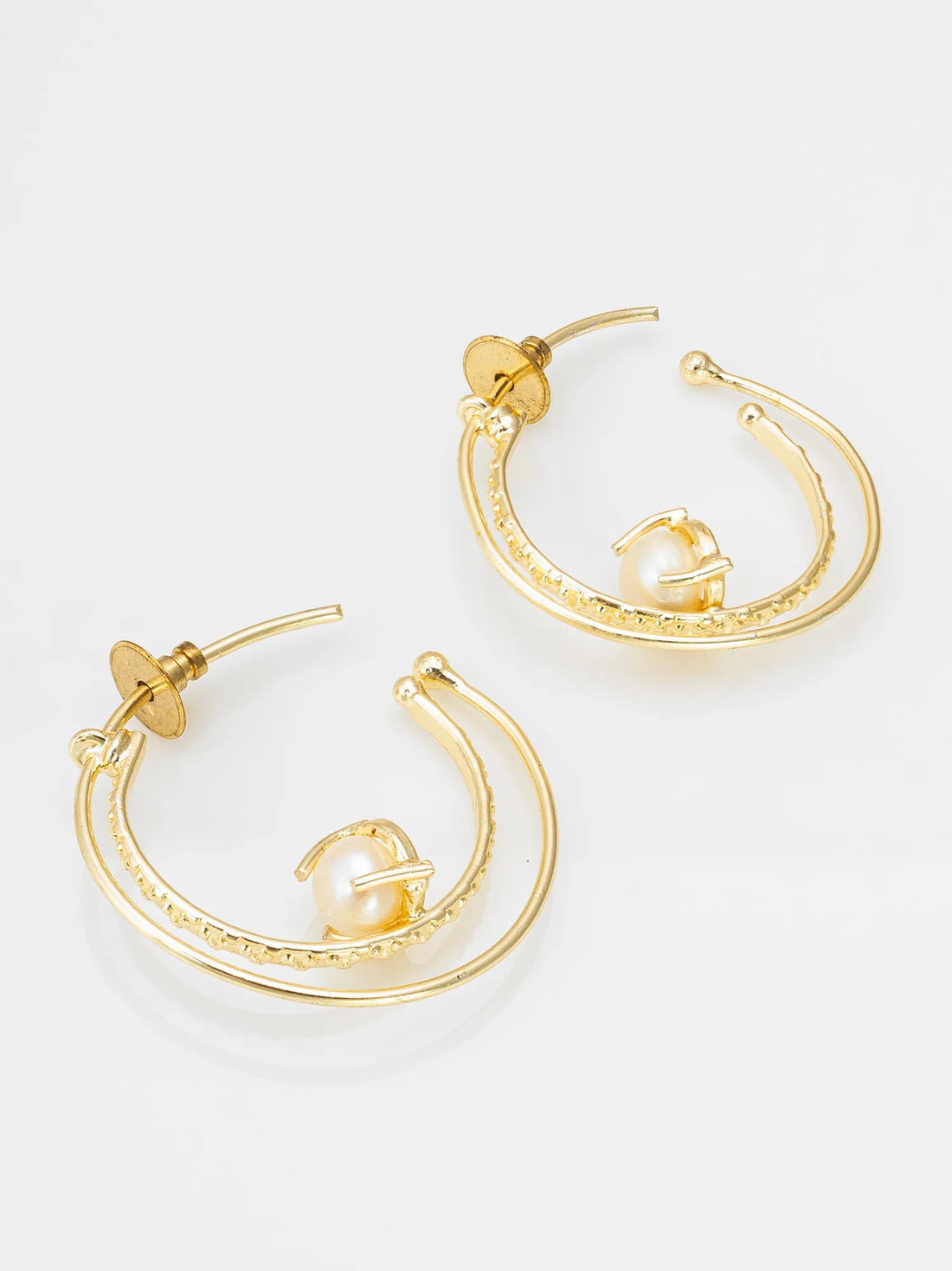 Gold hoop earrings with pearl-like beads on a red fabric background