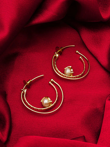 Gold hoop earrings with pearl-like beads on a red fabric background