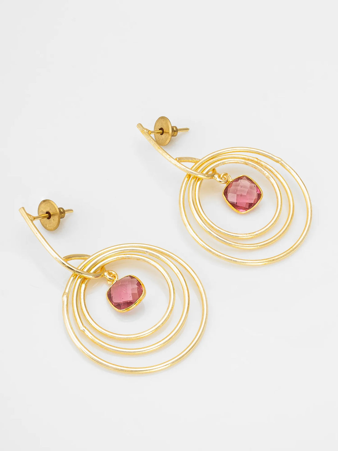 Gold hoop earrings with red gemstones on a red fabric background