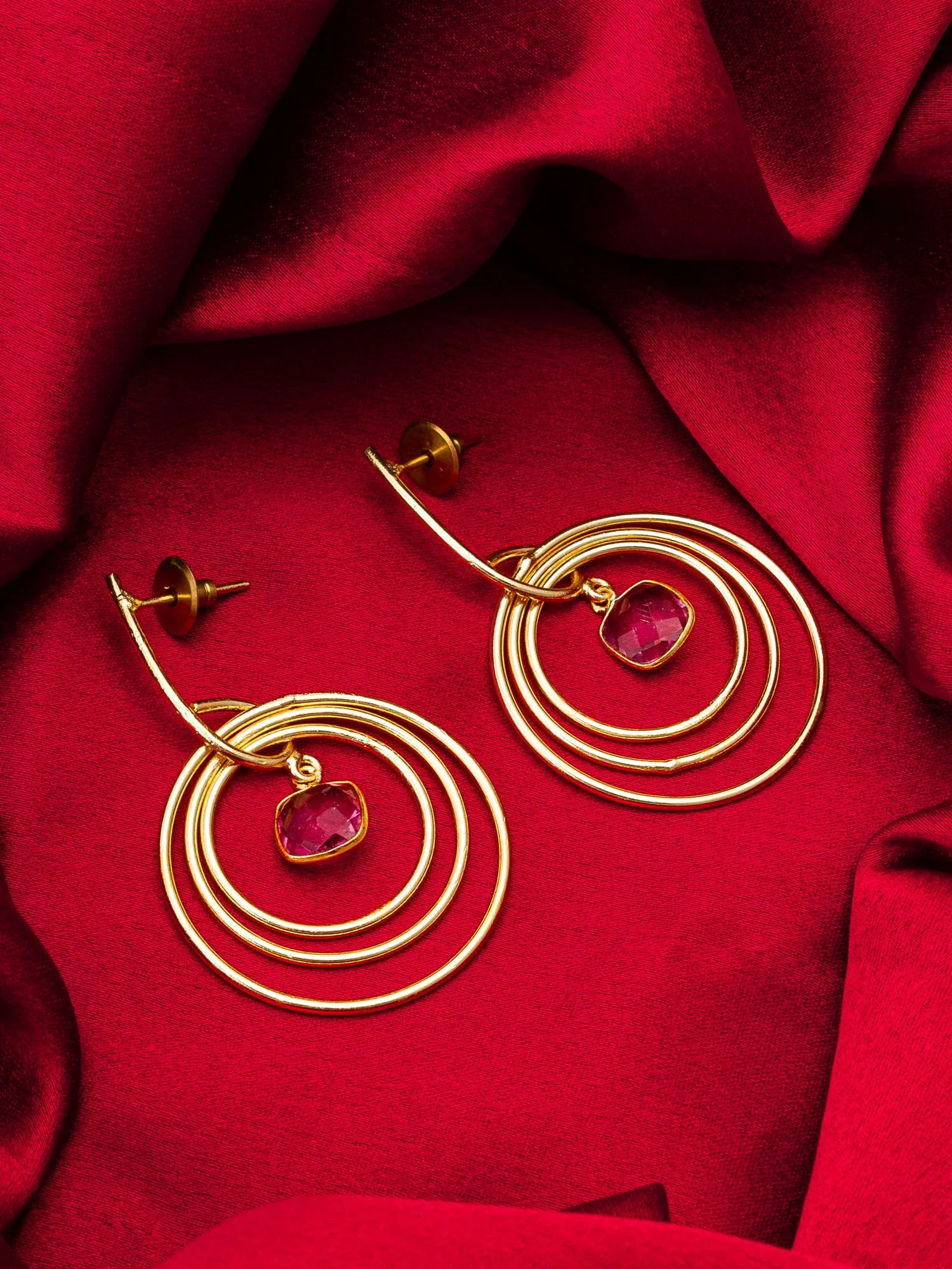 Gold hoop earrings with red gemstones on a red fabric background