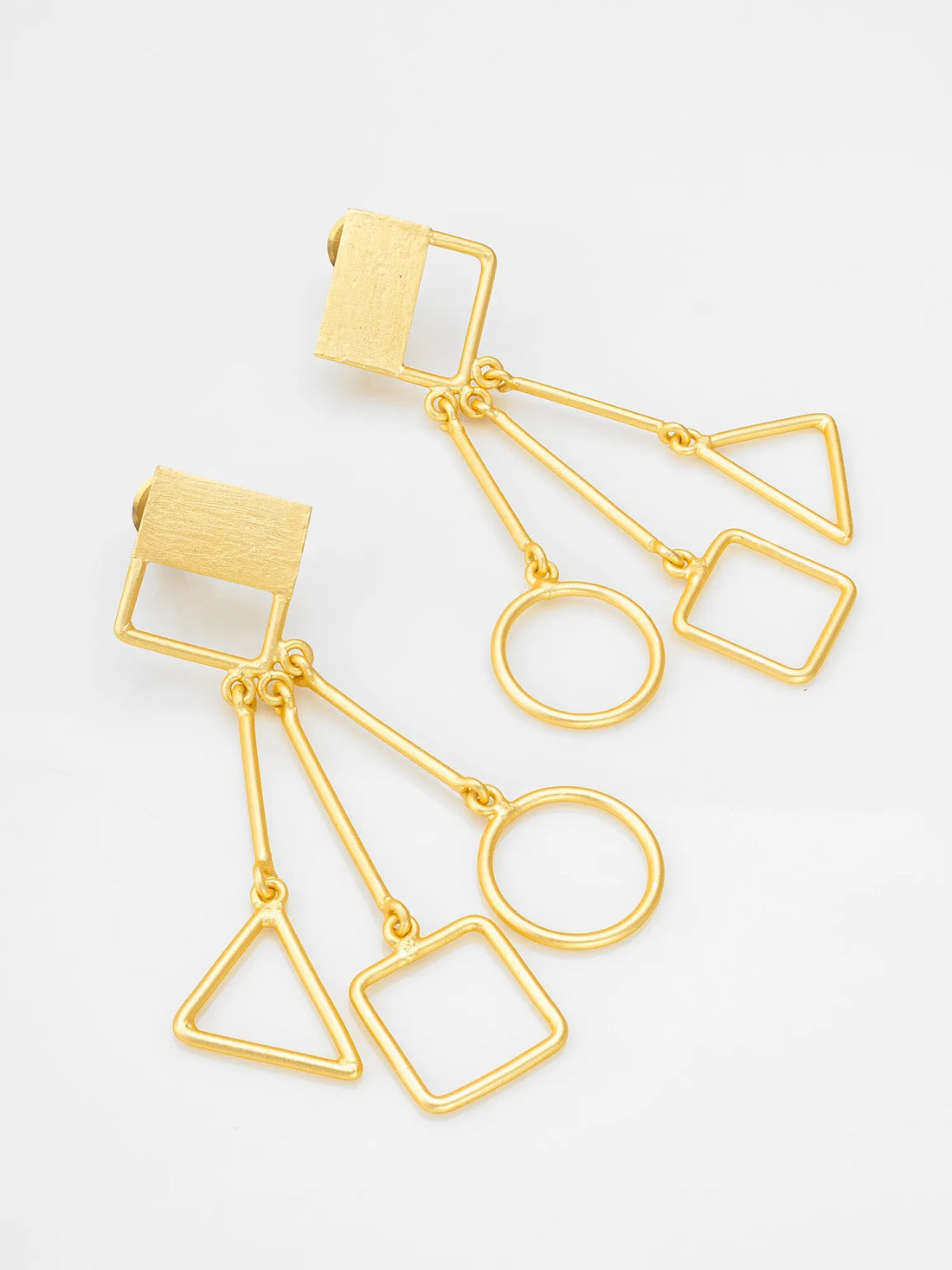 Gold geometric earrings on a red fabric background